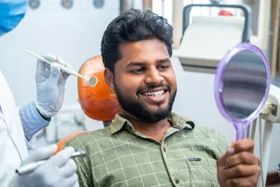 man smiling in the mirror during his dental appointment at Gina Biedermann DDS