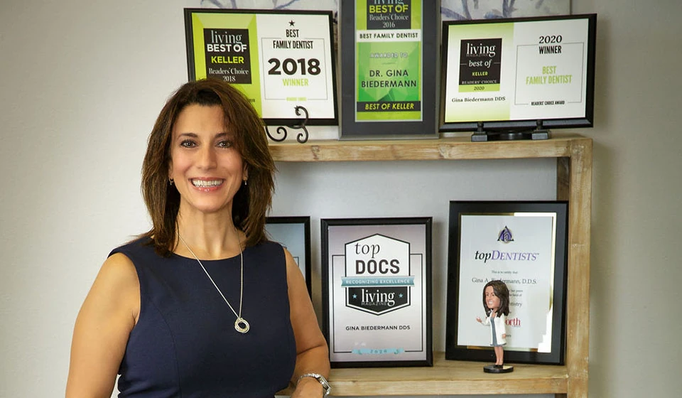 Dr. Gina Biedermann standing with her wall of awards for outstanding dental service