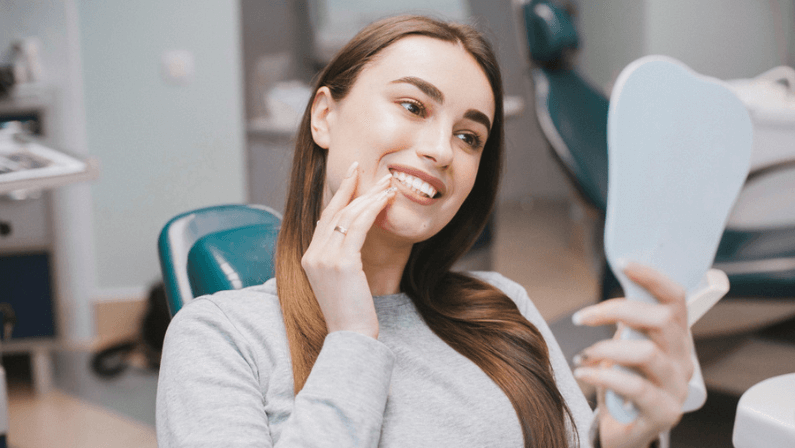 The girl smiles in dentistry. patient dentist racing model at the Dental Clinic. White well-groomed teeth after taking a doctor. Tooth whitening and tooth enamel. In the hands of the mirror