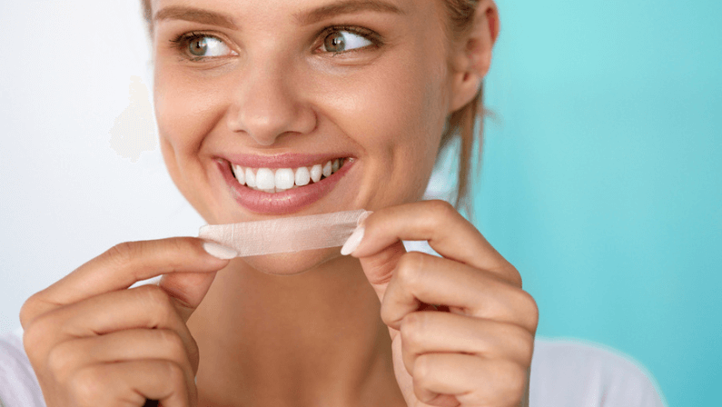 Healthy White Teeth. Beautiful Smiling Girl Holding Teeth Whitening Strip. Happy Young Woman With Perfect White Smile Using Dental Whitener. Dental Beauty, Tooth Care Concept. High Resolution Image