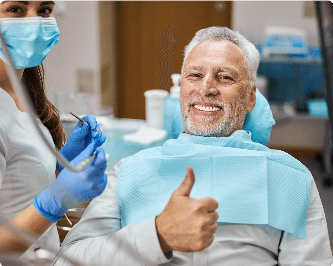 Senior man satisfied with dental restoration, giving thumbs up in dental chair