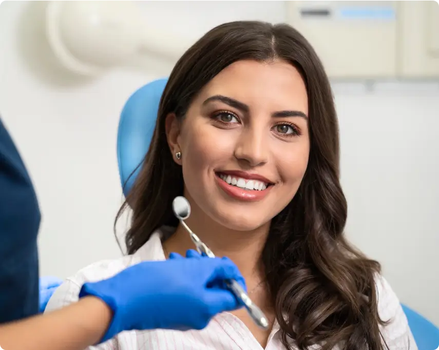 Dentist is about to examine smiling woman's teeth using dental mirror