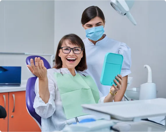 Middle-aged woman very happy while holding a mirror with dentist standing next to her