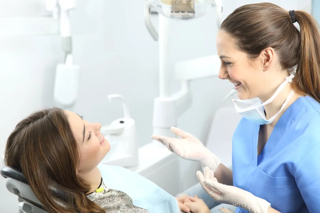 Relaxed young woman in dental chair converses with a friendly dentist, both beaming