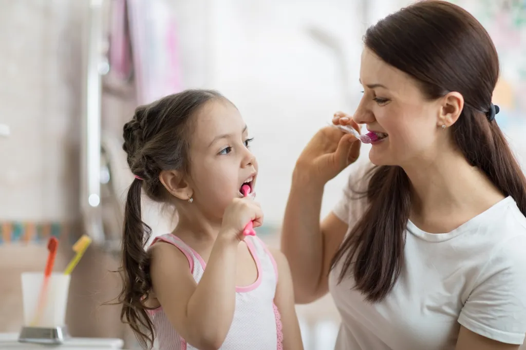 Mom patiently guides her daughter while brushing teeth together, fostering healthy dental habits from a young age.