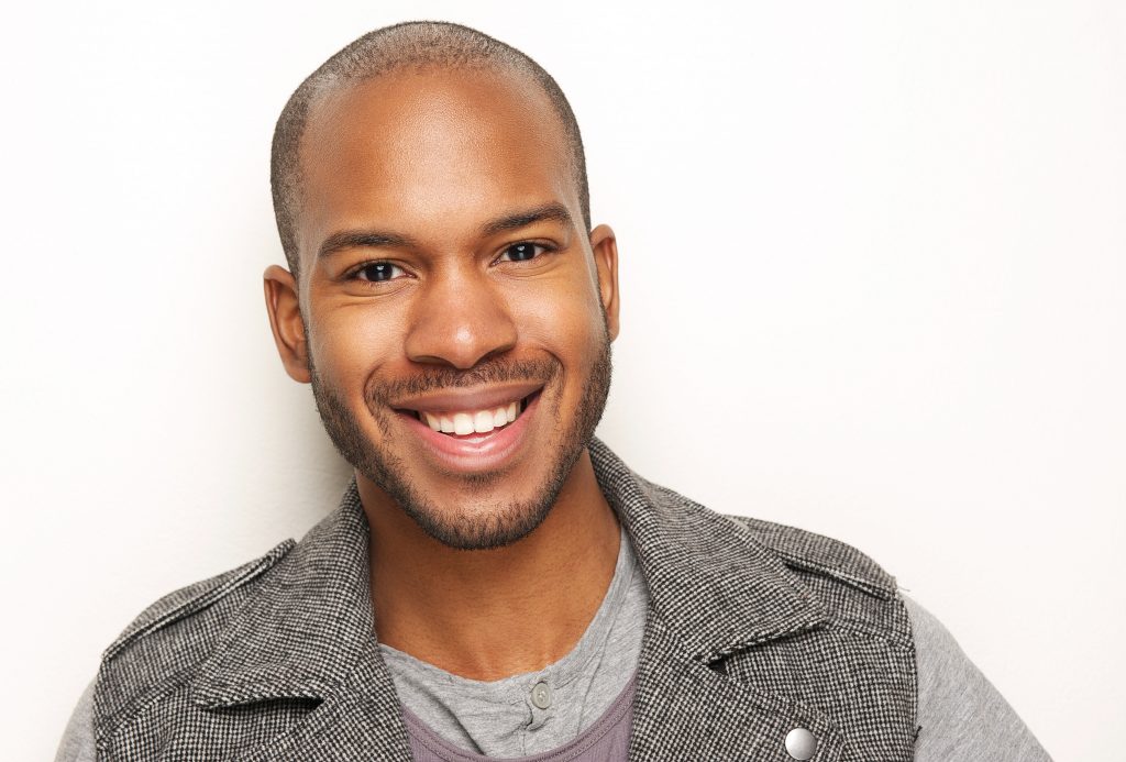 Black man beams with a confident smile, showcasing healthy teeth.