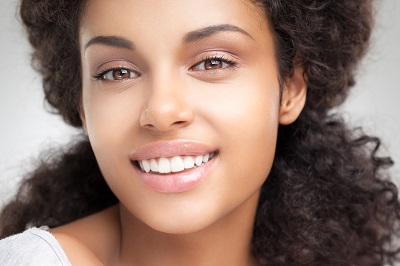 Young woman with curly hair flashes a radiant smile, showcasing her healthy teeth.