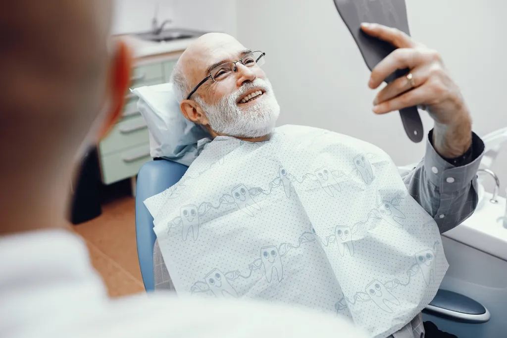 Senior man relaxed in dental chair, smiling confidently while examining his teeth in the mirror.