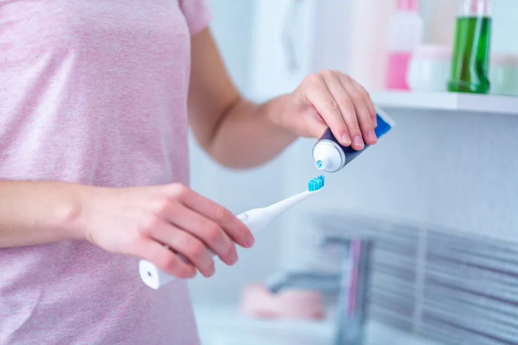 Woman's hands squeezing toothpaste onto a toothbrush.