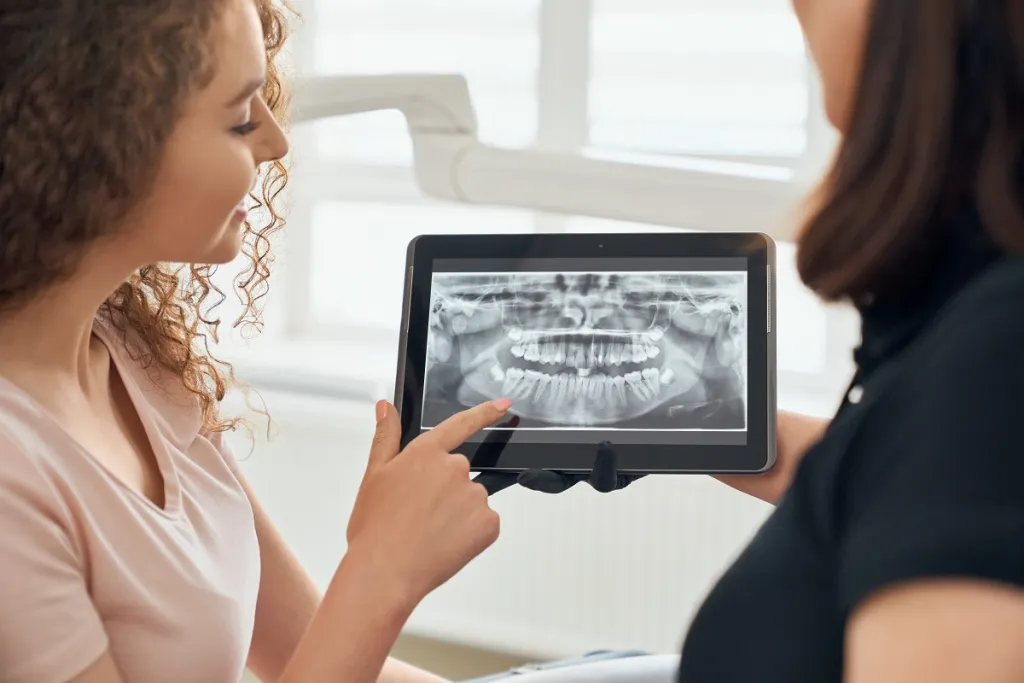 Dentist using tablet to show female patient her dental X-ray in modern dental office.