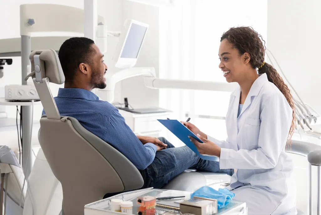 Black female dentist and male patient smiling during friendly consultation in modern dental office.