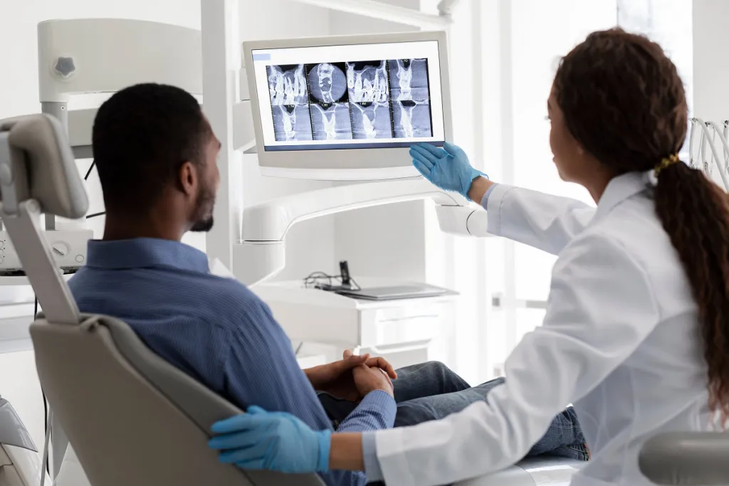 Black female dentist explaining dental X-ray to male patient in modern dental office.