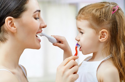 Female child and mother brushing teeth together, teaching good oral hygiene habits.