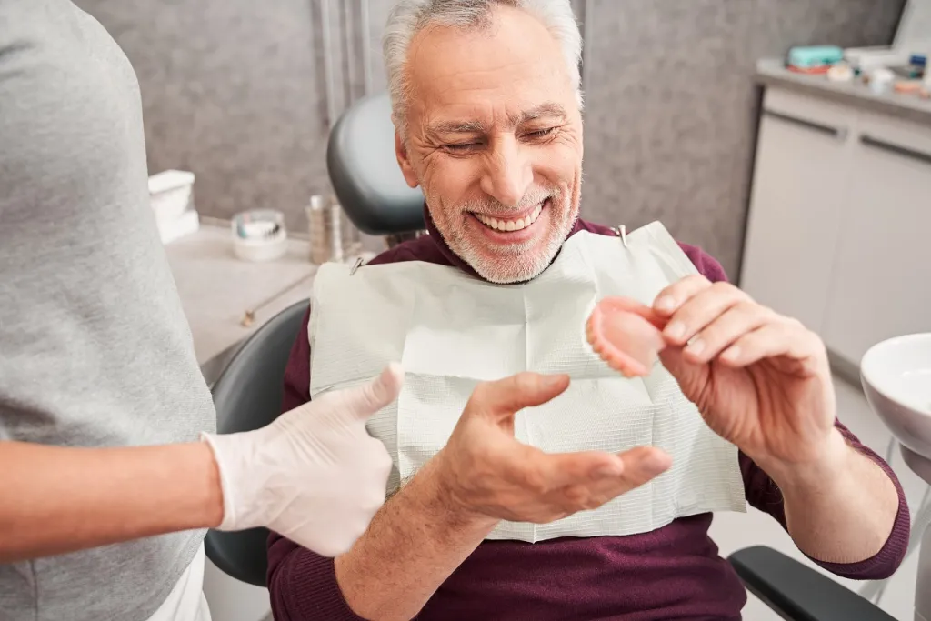 Senior man smiling with satisfaction while examining new dentures.