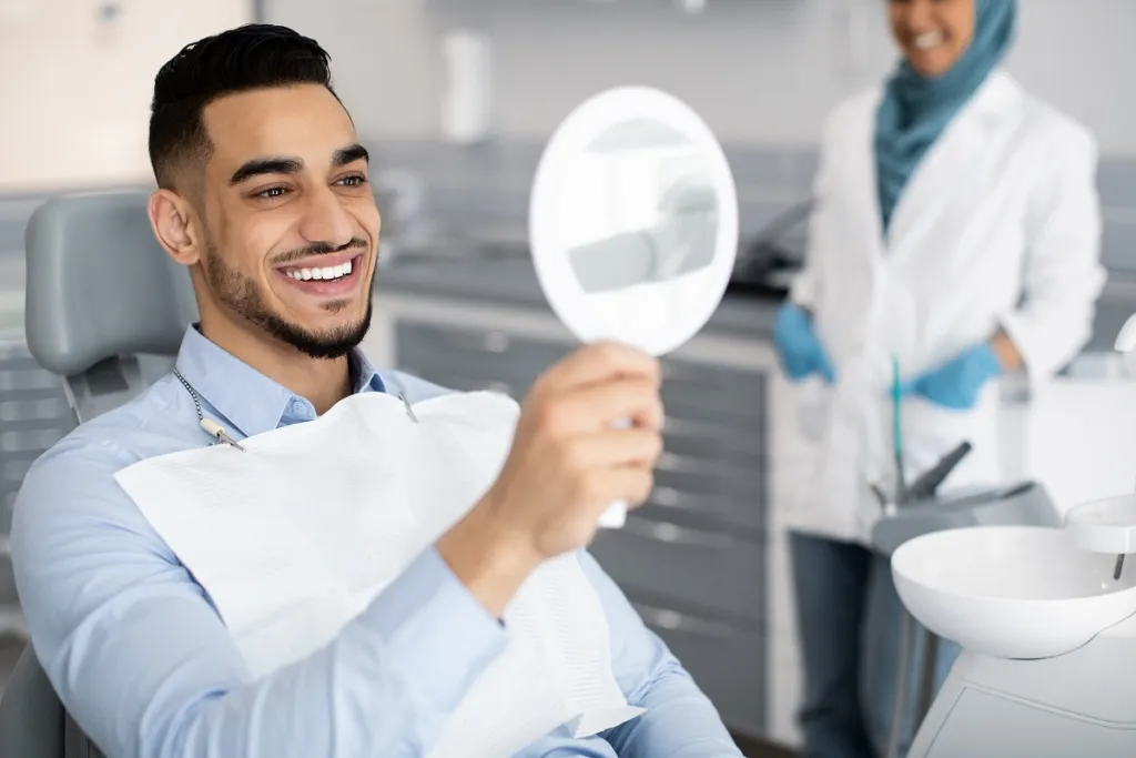 Man admiring his bright smile in mirror after successful dental treatment.