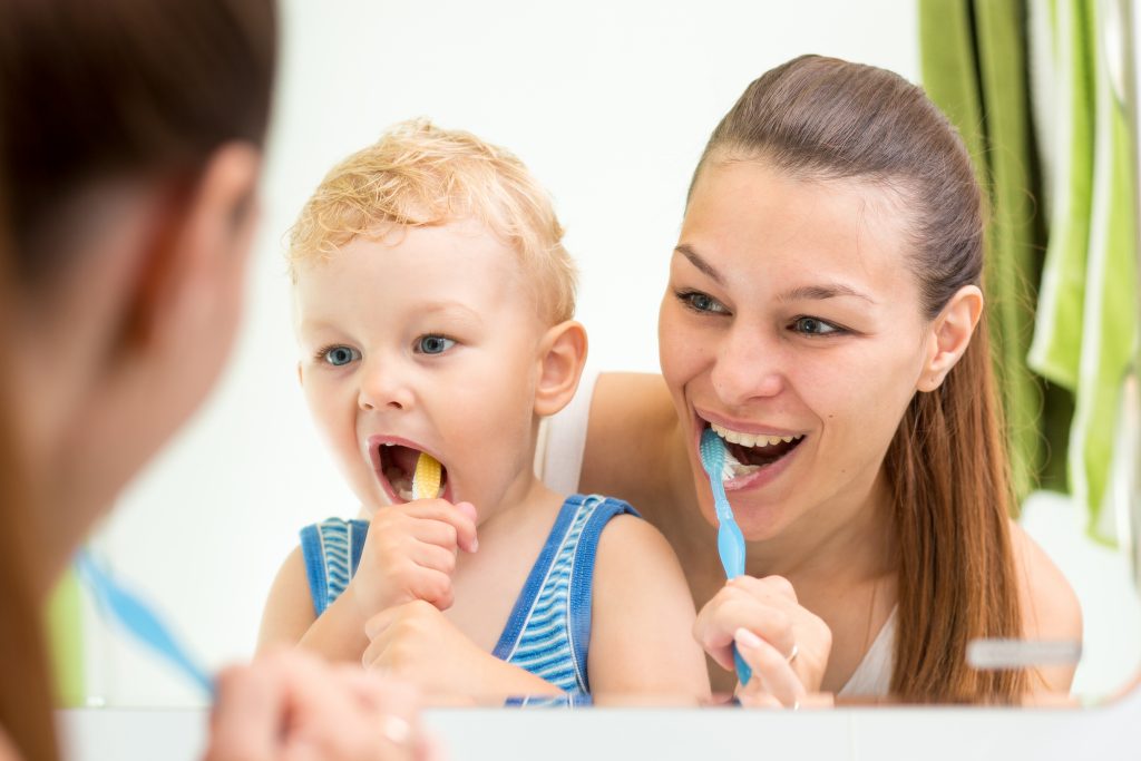 Mother and young boy brushing their teeth together in bathroom mirror, promoting healthy dental hygiene