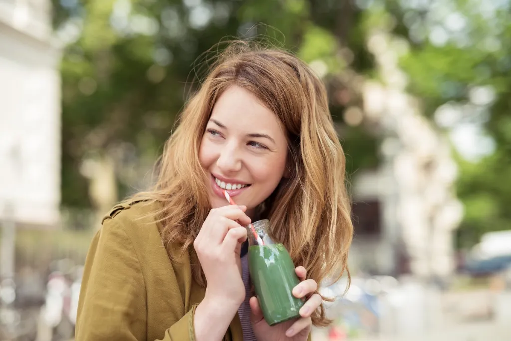 Smiling young woman enjoying a refreshing drink with a straw, showcasing healthy white teeth