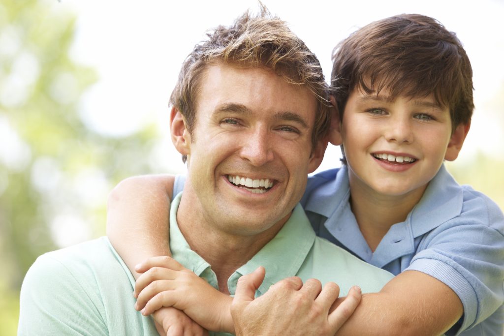 Happy young boy and father smiling together, showing off healthy white teeth