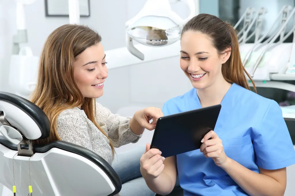 Female dental patient reviewing treatment plan with dentist on digital tablet