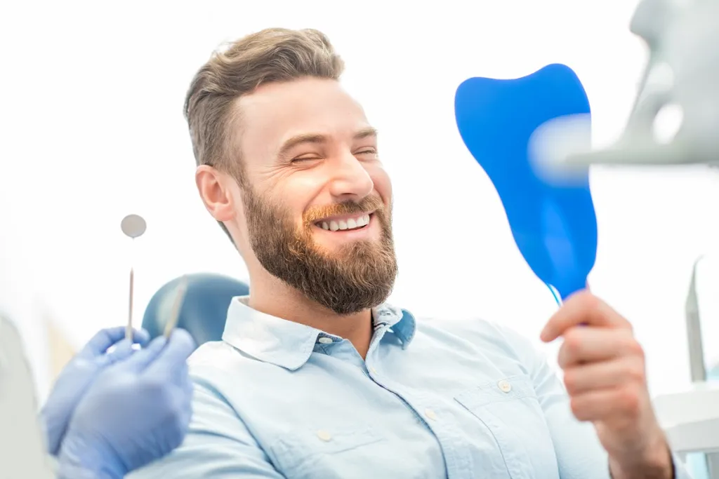 Middle-aged man with bright smile after dental procedure checking teeth in mirror