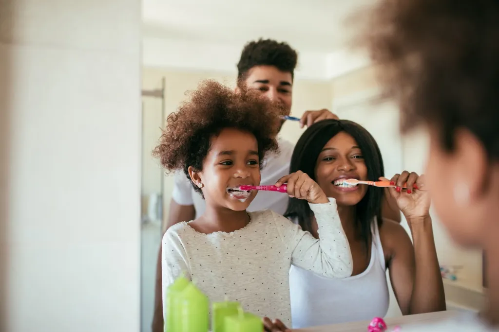 Happy family brushing teeth together in bathroom mirror, promoting healthy dental hygiene