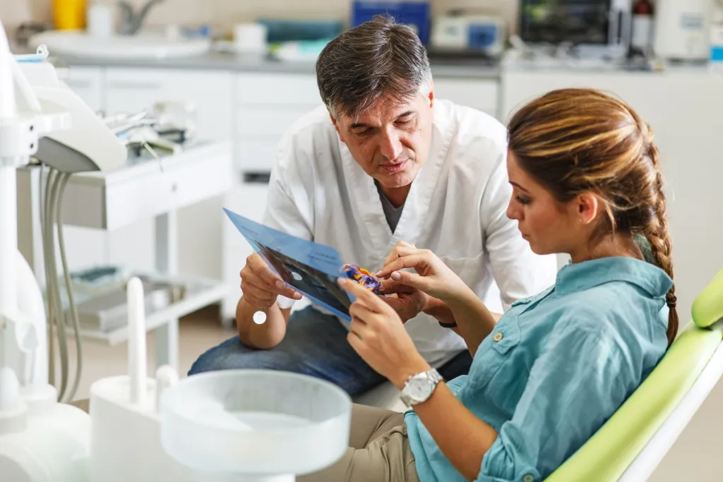 Male dentist explaining dental X-ray to patient in reclining dental chair