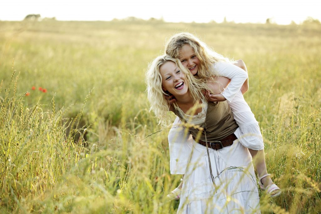 Joyful mother piggybacking her smiling daughter with bright smiles in a sunny field.